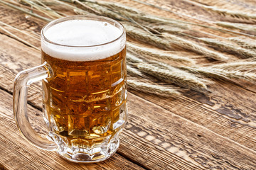 Glass of beer with ears of barley on a wooden background.