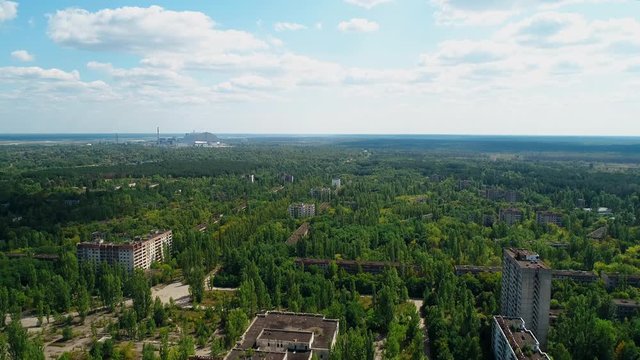 Aerial view of abandoned buildings and streets overgrown with trees in city Pripyat near Chernobyl nuclear power plant. Exclusion Zone. Camera moves away. Sign of USSR on the roof. 4K drone footage.