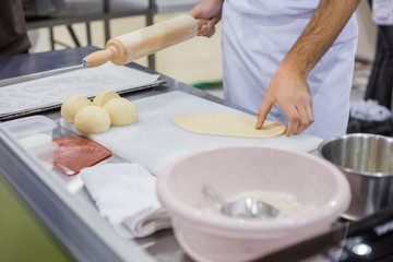 Obraz na płótnie Canvas Baker, chef hands preparing fresh dough with rolling pin on kitchen table at cuisine of restaurant, bakery. Professional cooking, catering, culinary, gastronomy and food concept