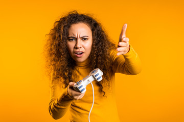 Pretty young girl playing video exciting game on Tv with joystick on yellow studio wall. Using modern technology.