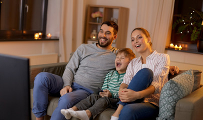 family, leisure and people concept - happy smiling father, mother and little son with remote...