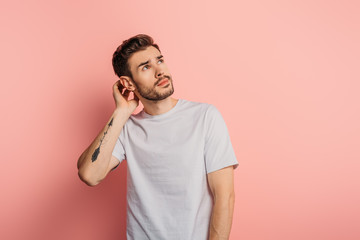 dreamy young man touching head and looking up on pink background