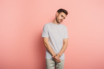 offended young man looking at camera while standing on pink background