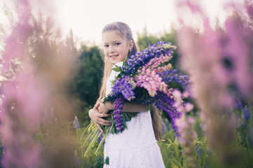Cute girl with long hair in a white dress with flowers in her hands on nature