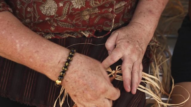 Senior caucasian female weaving basket on the craft workshop. Close up video of woman's hands making handicraft