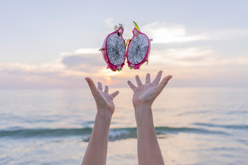 female hands throw up two pieces exotic dragon fruit, behind sea on sunset time, summer, tropical. Photo is ideal for advertising, poster and wallpaper