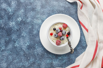 Rice pudding with frozen blueberries and raspberries in white bowl