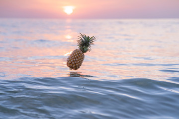 Juicy beautiful thai pineapple falls into the water at sunset. Pineapple is hovering over the sea...