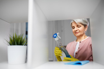 people, housework and housekeeping concept - happy senior woman cleaning rack and reading label on detergent at home