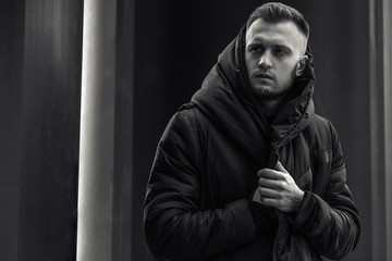 A guy, a model with brown hair in a black coat, black jeans and sneakers, posing against a...