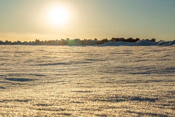 snow-covered field with hummocks, the sun setting over the horizon on a winter evening