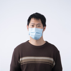 Young Asian man portrait, feeling sick, wearing a surgical blue face mask to prevent infection, air pollution isolated on white background, cut out.