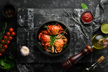 Boiled sea crabs with vegetables in a black pan. Seafood. Top view. Free space for your text.