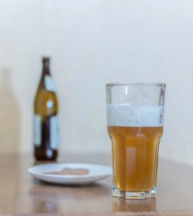 Beer in a glass on a wooden table in the background a bottle