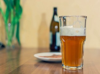 Beer in a glass on a wooden table in the background a bottle
