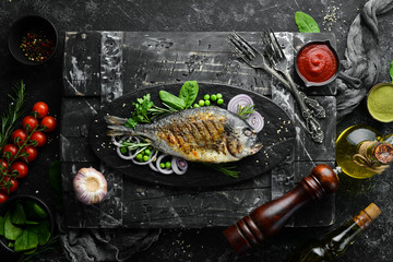 Baked Dorado fish with vegetables on a black stone plate. Top view. Free space for your text.
