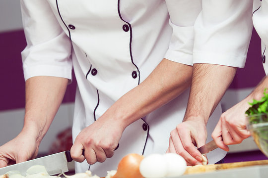 Cooking process concept. Hands of two working men in cook uniform making food in modern kitchen. Close up. Indoor shot