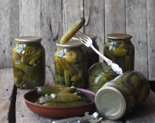 The benefits and harms of canned pickled cucumbers. Pickled cucumbers on a fork and in cans on a wooden ancient background. Side view, place for text.