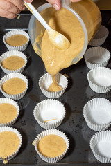Top view of person pouring dough for cinnamon muffins in paper molds on baking sheet, in cooking class, in vertical