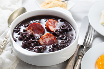 typical brazilian food black beans with smoked sausages in white bowl