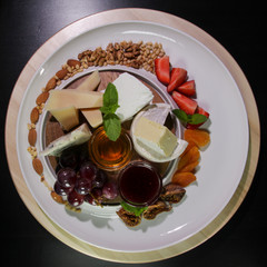 Cheese plate.Isolated on a black background.Camembert cheese, Parmesan, blue cheese served with grapes, jam, figs, honey, strawberries, dried apricots and nuts on a white plate.View from above.