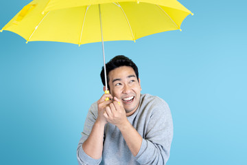 Happy Asian man holding yellow umbrella on blue background. © nuiiko