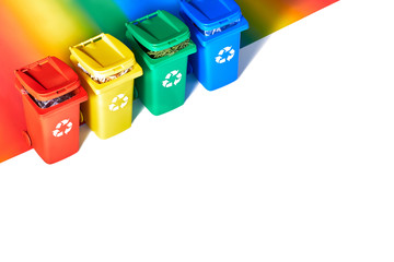 Four color coded recycle bins, isometric projection on geometric rainbow paper background with copy-space. Recycling sign on the bins - red,  blue, yellow and green. Waste separation, geometric