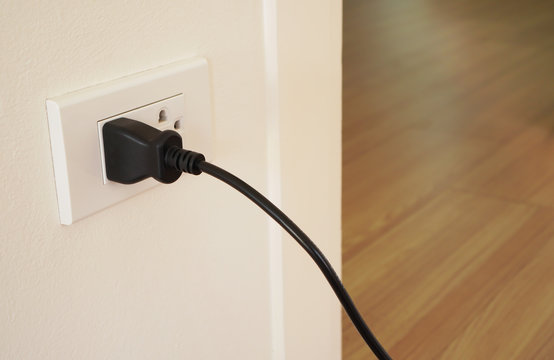 black plug of electrical appliance or device is plugging in the electric socket on white wall, power saving or cost reduction concept
