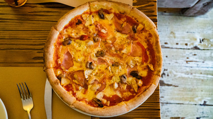 Pizza with Mozzarella cheese, ham, tomato sauce, salami, pepper, Spices and Fresh arugula. Italian pizza on wooden table background