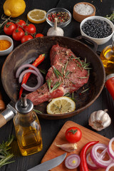 Raw beef antricot on a wooden board. Composition with rosemary, hot pepper and other spices for cooking meat. A look from above. close-up