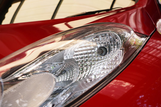 headlight in left side of red automobile ,show headlight bulb inside, photo shooted during day time under car parking shade