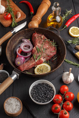 Raw beef antricot on a wooden board. Composition with rosemary, hot pepper and other spices for cooking meat. A look from above. close-up