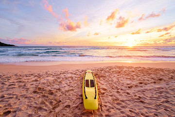 Beautiful landscape. Sunset on the sea beach with lifeguard surf board on sand.