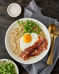 Oatmeal, fried egg and fried bacon. Brutal man sport protein breakfast. Balanced food. Vertical