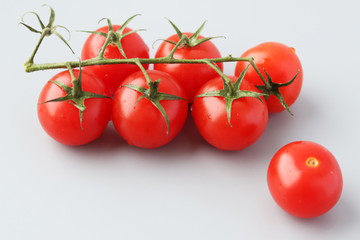 Beautiful red tomatoes on a green branch on a gray background and next to one tomato. Selective focus on vegetables.