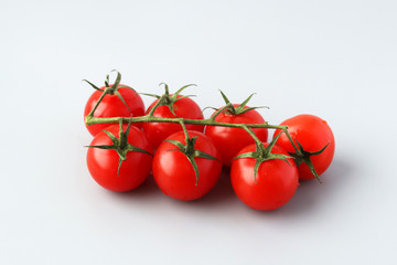 Red delicious fresh cherry tomatoes on a green branch on a light background. The branch with the tomatoes. Selective focus on tomatoes and greens. Useful vitamin food. Vegetarianism