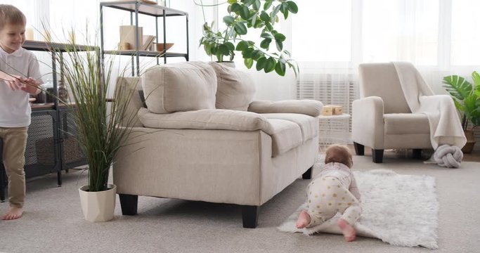 Happy boy running while playing hide and seek game with his cute baby sister in living room