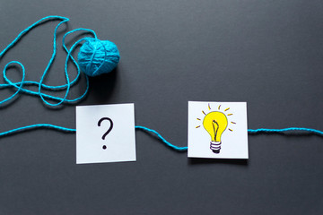 Question mark and light bulb drawn on notes and a ball of thread on the dark background.