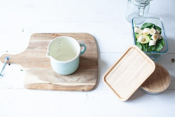 Wooden cutting board with chia seed, banana, spinach and avocado and a knife and glass jars on white wooden background 