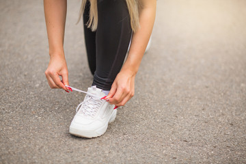 woman ties a lace on a white sneaker