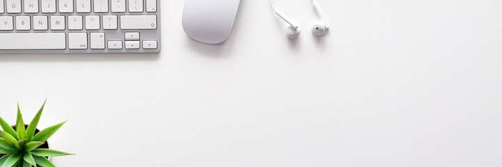 Top view of a white office desk. Copy space. White technology. Keyboard, mouse, headphones and succulent. White on white. Copy space. Panorama