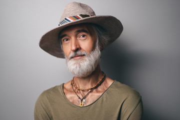 Style and vacation concept. Studio portrait of handsome senior man with gray beard and hat.