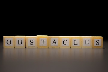 The word OBSTACLES written on wooden cubes isolated on a black background...