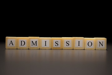 The word ADMISSION written on wooden cubes isolated on a black background...