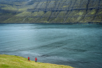 Two female hikers walking on a trail next to a wide fjord in Faroe Islands.