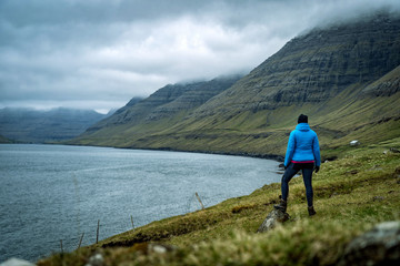 Fototapeta na wymiar Female traveler standing at top of mountain and enjoying spectacular view over Faroe Islands fjords.