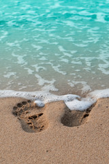 Two footprints on a sandy beach with waves and bubbles of sea water
