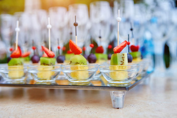 Fruit canapes on a glass tray, on the background of wine glasses and champagne. Catering concept