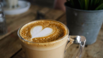 Foam with a heart for cappuccino coffee. Coffee in a transparent cup on a wooden table.