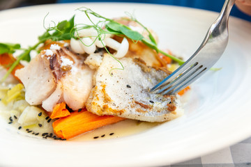 Delicious fillet of cod fish with carrots, leeks and mushrooms in white plate ready to be served
